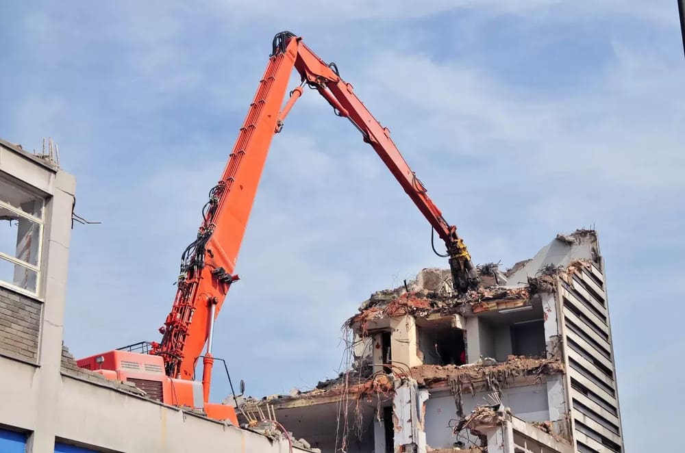 A crane is lifting rubble from the side of a building.